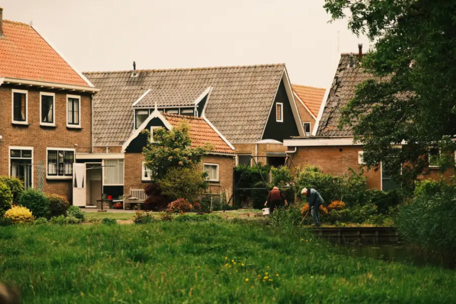 Bewoners aan het werk in groene achtertuinen achter Nederlandse rijtjeshuizen, met gras en borders als regenbestendige tuin