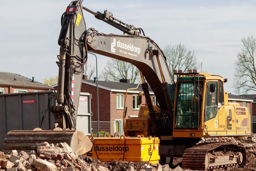 Yellow excavator on a building site next to Dutch terraced houses, the kind of digging that needs a KLIC notification
