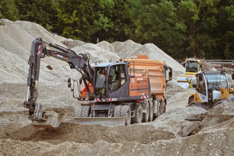 Graafmachine tussen bergen zand en grind op een bouwterrein, zoals gebruikt bij het ophogen van zettingsgevoelige grond