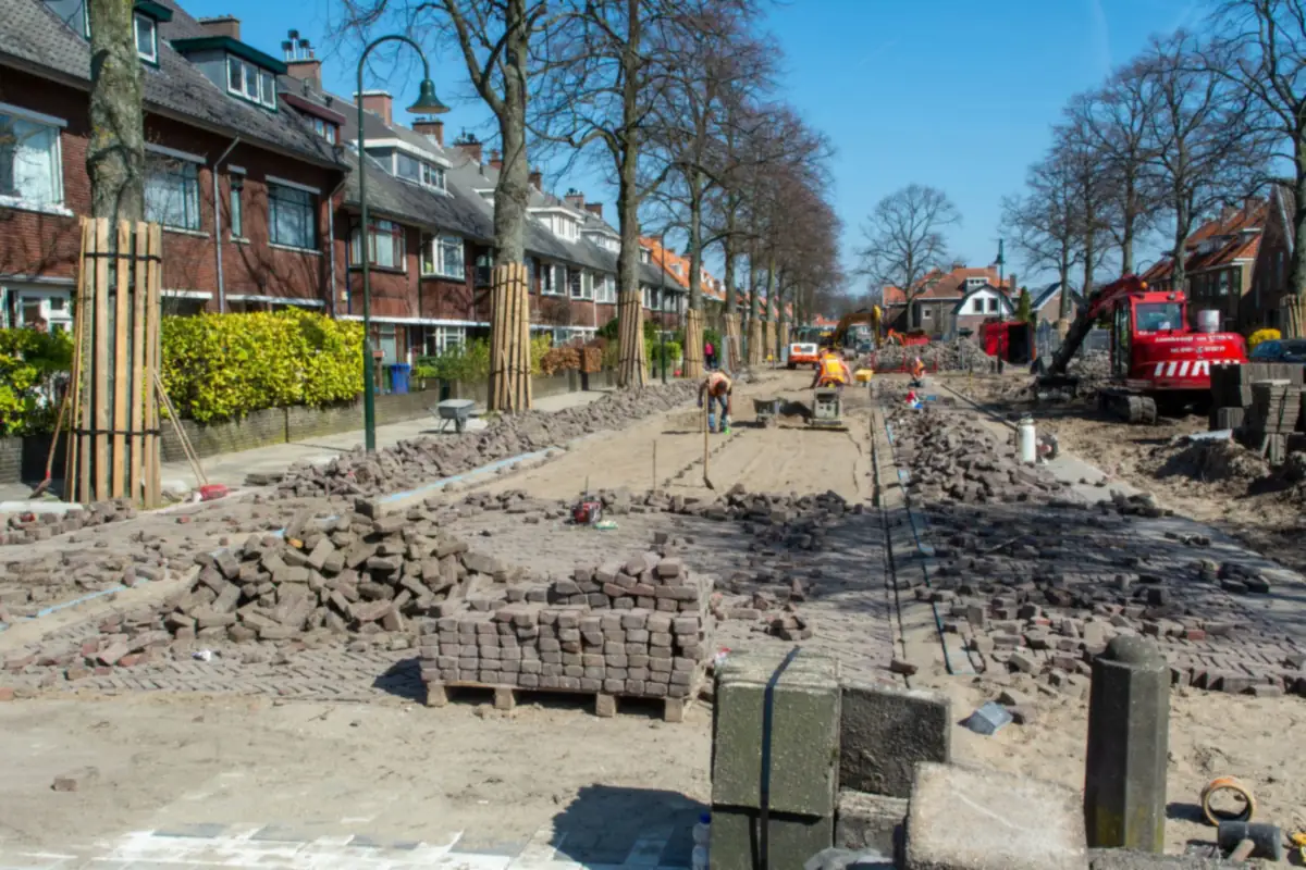 Opgebroken klinkerstraat met pallets nieuwe klinkers en een trilplaat, zoals bij het ophogen van verzakte bestrating in Amsterdam